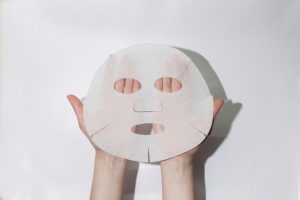 Sheet face mask. Fabric mask for facial skin. Female hands hold